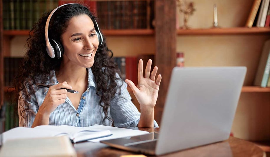 Woman sitting at desk, using computer and waving to webcam