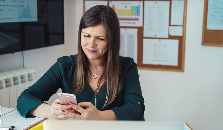 female school teacher using cellphone at her desk