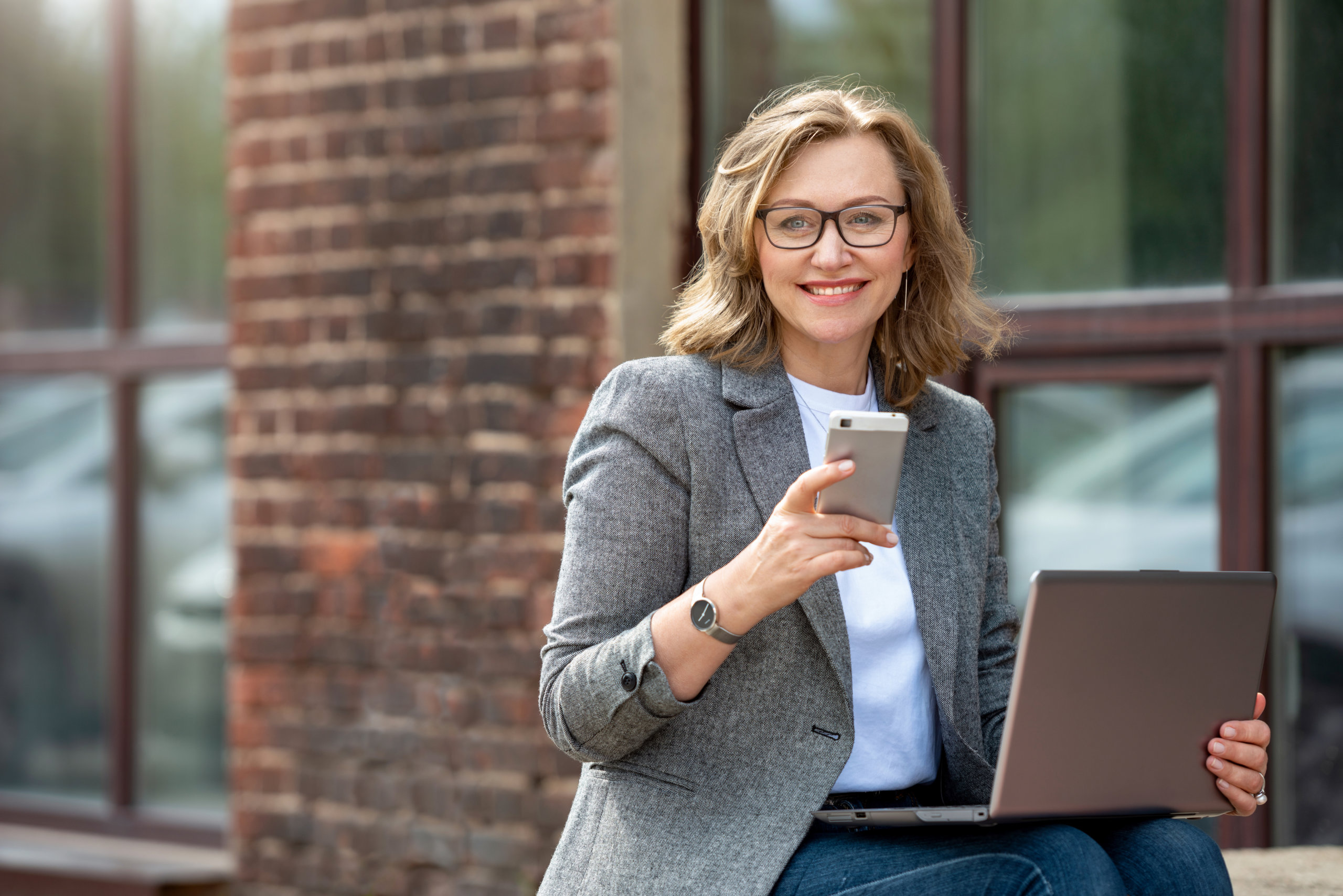 woman on her cell phone and laptop outside building