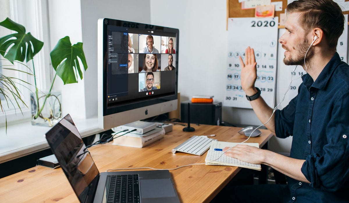 guy working from home waving to colleages on video conference chat